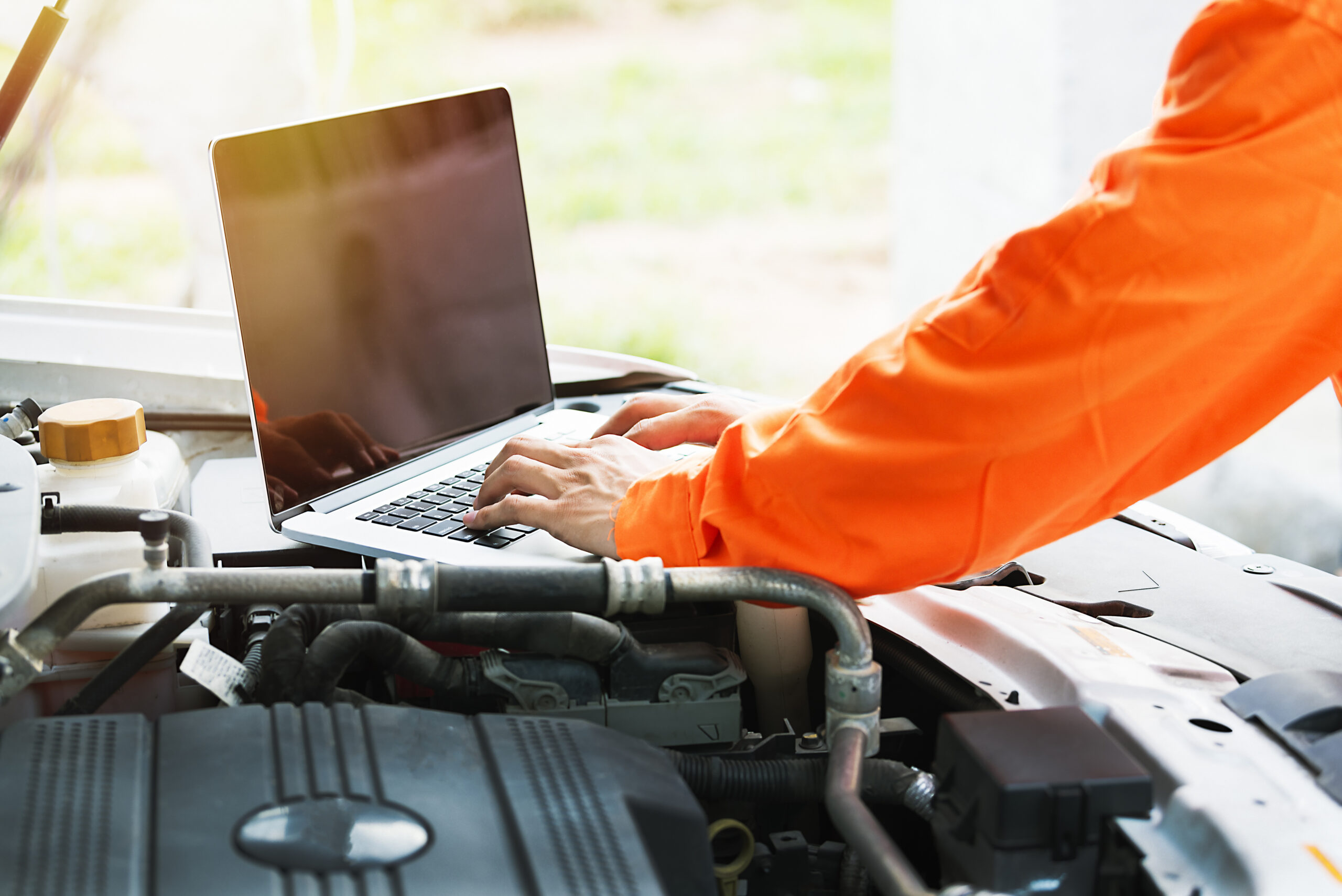 En laptop som står på en bilmotor och en person som använder laptopen